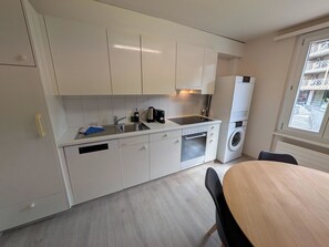Una cucina compatta con mobili bianchi, lavello, macchina da caffè, lavastoviglie e una lavatrice integrata.