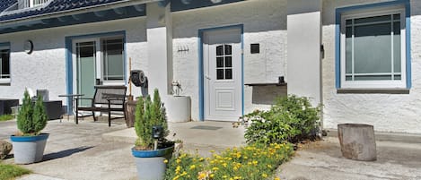 A two-story house with a balcony, a door, and a window. There is a bench and a potted plant in the front yard.