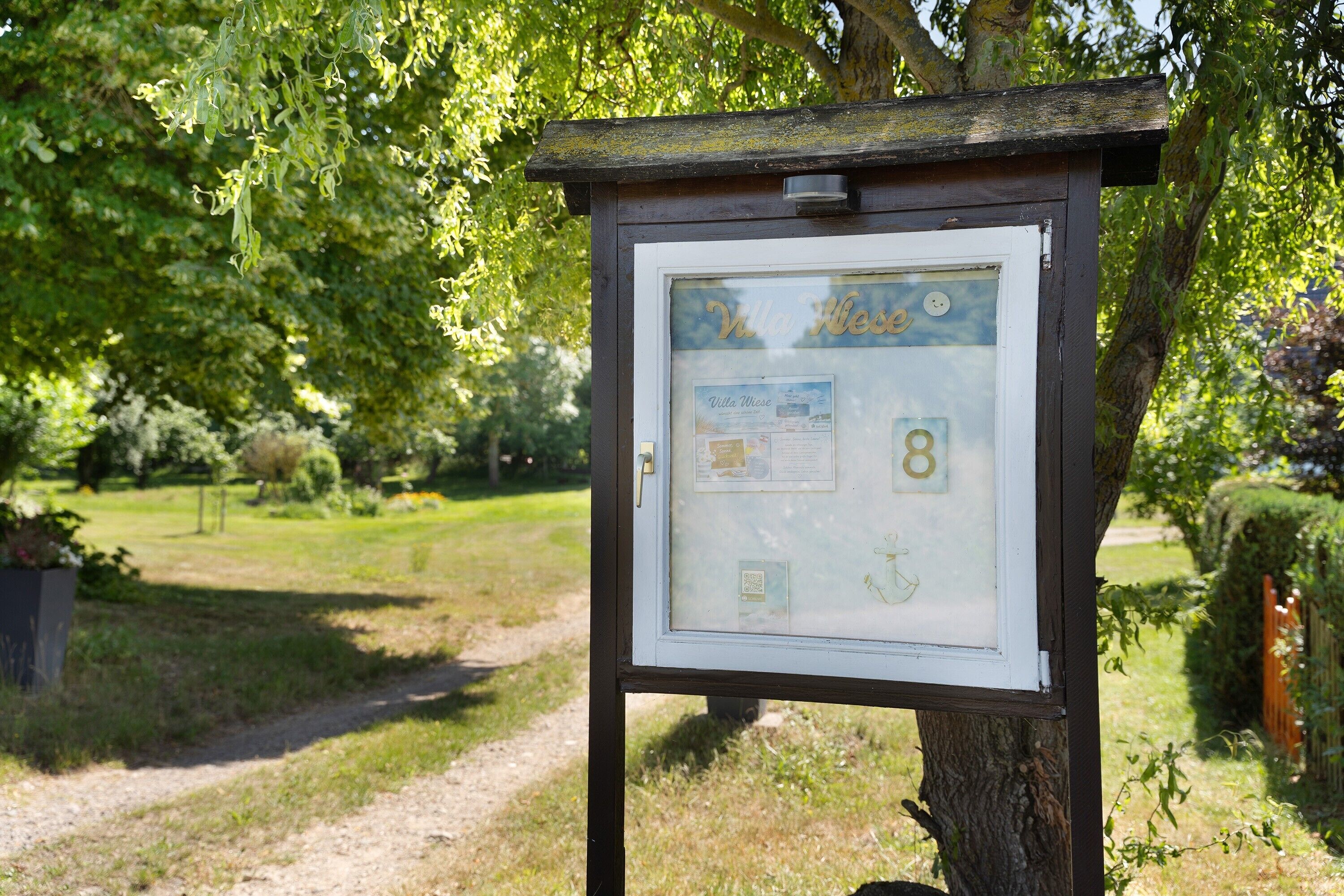 Un panneau indicateur en bois, doté d’un cadre et d’une surface d’affichage contenant des informations, entouré de verdure et bordé d’un sentier.