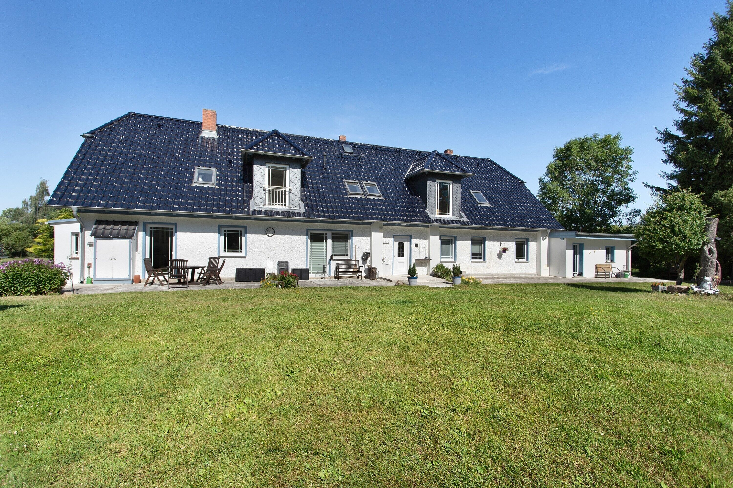 Ein zweistöckiges Haus mit geneigtem Dach, einer Veranda mit Tisch und Stühlen und einem gepflegten Rasen.