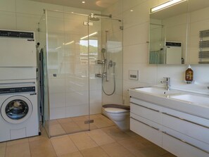 Ein modernes Badezimmer mit einer Glaskabine zur Dusche, einer integrierten Waschmaschine und einem Waschbecken mit Spiegel darüber.