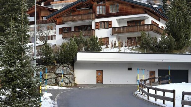 A multi-story building with wooden balconies, a stone wall, and a paved driveway. - Chesa Igna Appartement/Fewo, Bad, WC, 4-Bettwohnung by Interhome (Arosa)