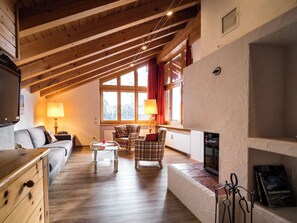 Ein gemütliches Wohnzimmer mit Kamin, Holzbalken und großen Fenstern.