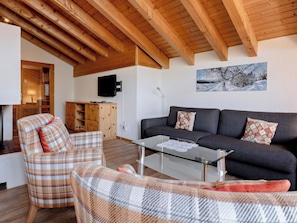A living room with a sofa, a glass coffee table, a plaid armchair, wooden beams on the ceiling, and a painting on the wall. - Tschuggenweg 14 Appartement/Fewo, Bad, WC, 5-Bettwohnung 5-Bettwohnung by Interhome (Arosa)