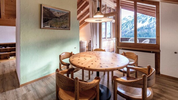 Een houten eettafel met zes stoelen, een hanglamp en een schilderij aan de muur.