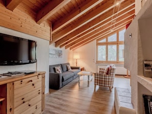 A cozy living room with a wooden ceiling, a flat-screen TV, a sofa, a coffee table, and a plaid armchair. - Tschuggenweg 14 Appartement/Fewo, Bad, WC, 5-Bettwohnung 5-Bettwohnung by Interhome (Arosa)