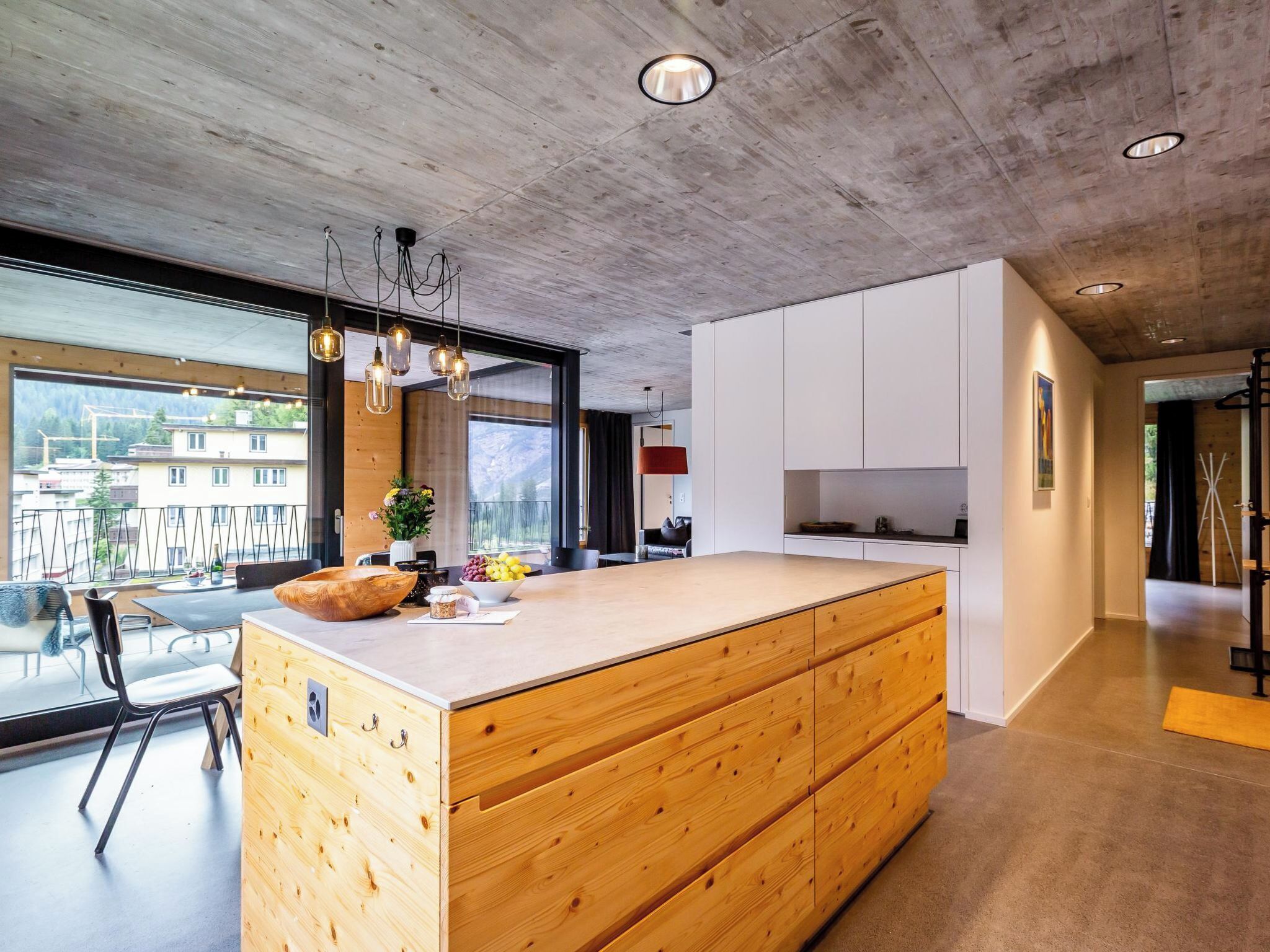 A modern kitchen with a wooden island, large windows, and a view of the outside.