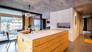 Een moderne keuken met een houten kookeiland, grote ramen en uitzicht op buiten.