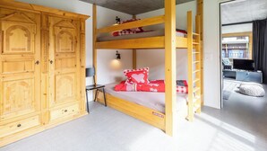 Een stapelbed met een ladder, een houten garderobe en een klein bureau met stoel.