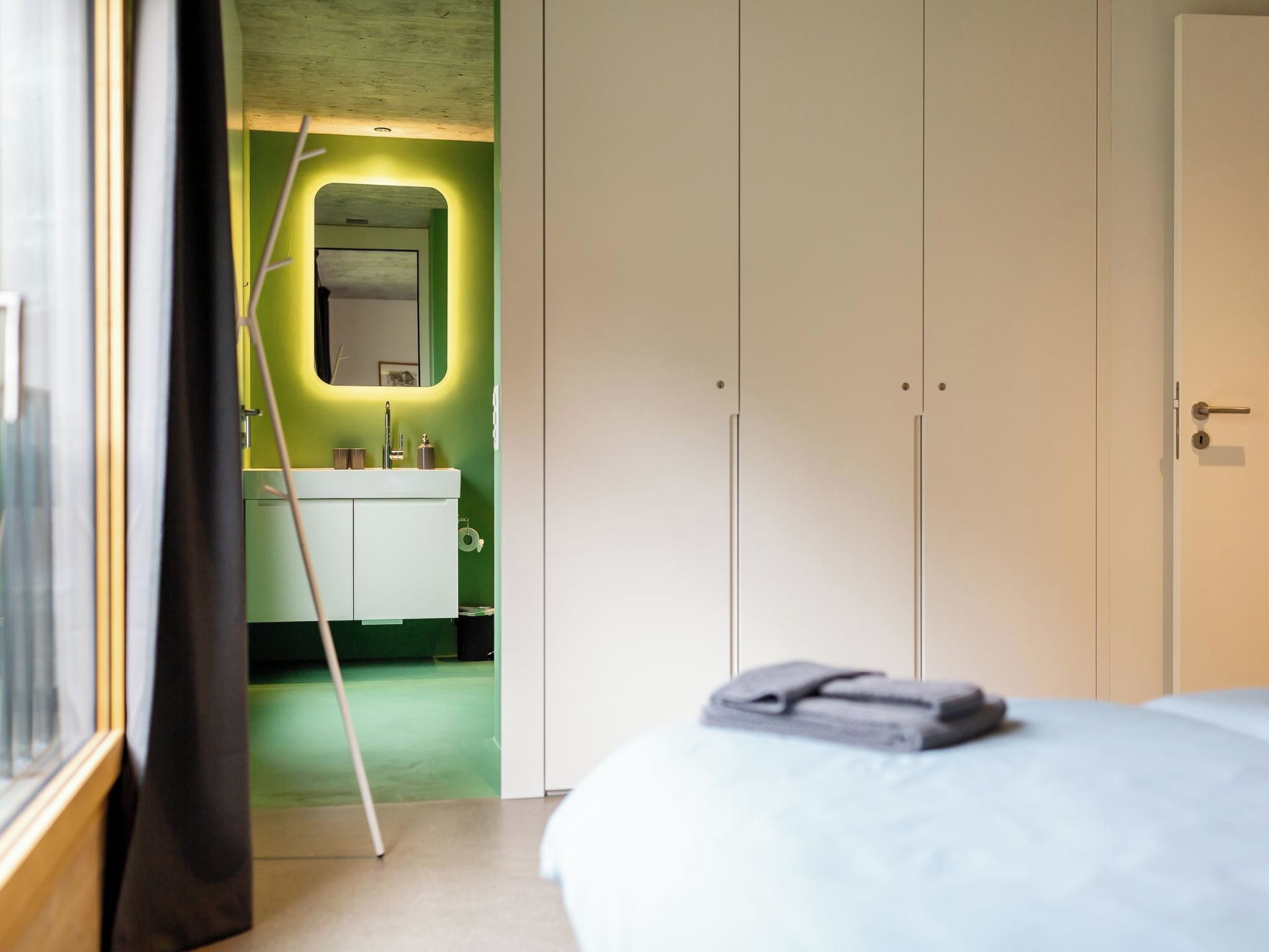 A hotel room with a bed, a bathroom with a mirror, and a door leading to another room.