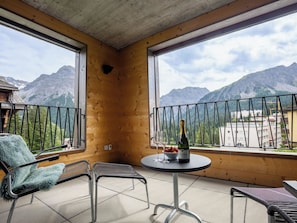 Ein Balkon mit Bergblick, zwei Stühle, ein Tisch mit Flasche und Gläsern sowie eine Holzwand.