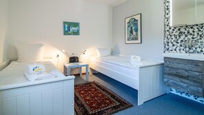 Hotellihuone, jossa on kaksi sänkyä, pieni pöytä, yöpöytä, peili ja kuviollinen seinä.