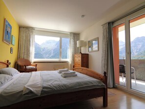 A bedroom with a bed, a chair, a dresser, and a window with a mountain view. - Casa Linda 7 by Arosa Holiday Appartement/Fewo, Dusche, WC, Balkon Linda 7 by Interhome (Arosa)