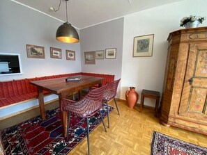Ein Essbereich mit einem Holztisch, einer rot gepolsterten Bank, gemusterten Teppichen und einer Holzkommode.