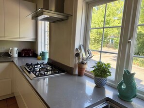 A kitchen with a gas stove, a coffee maker, a toaster, and a window with a view of greenery. - Avenue Road (Lymington)