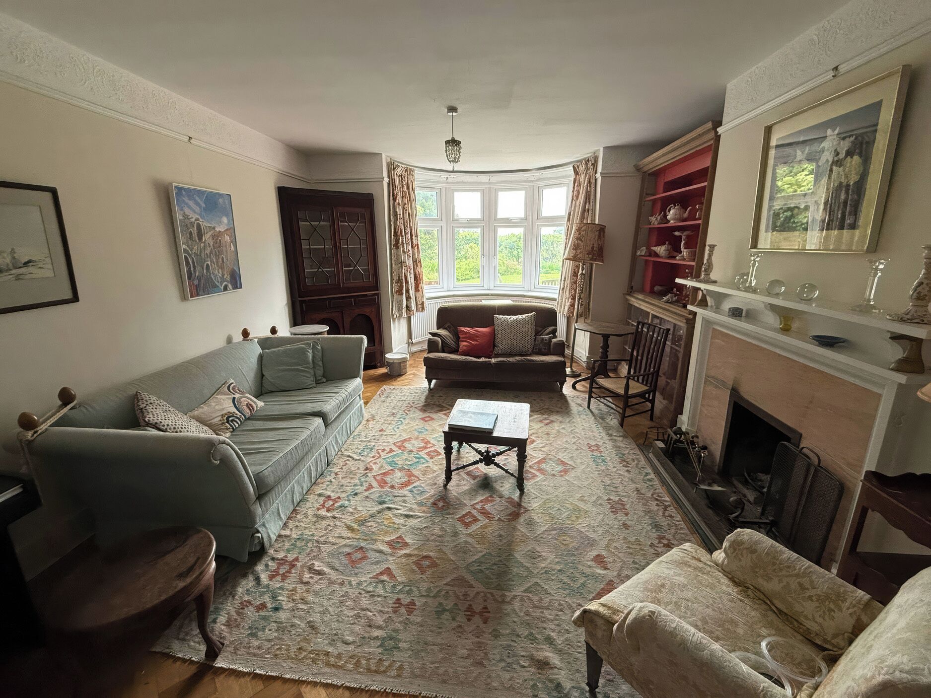A traditional living room with a sofa, armchair, fireplace, and a large window.