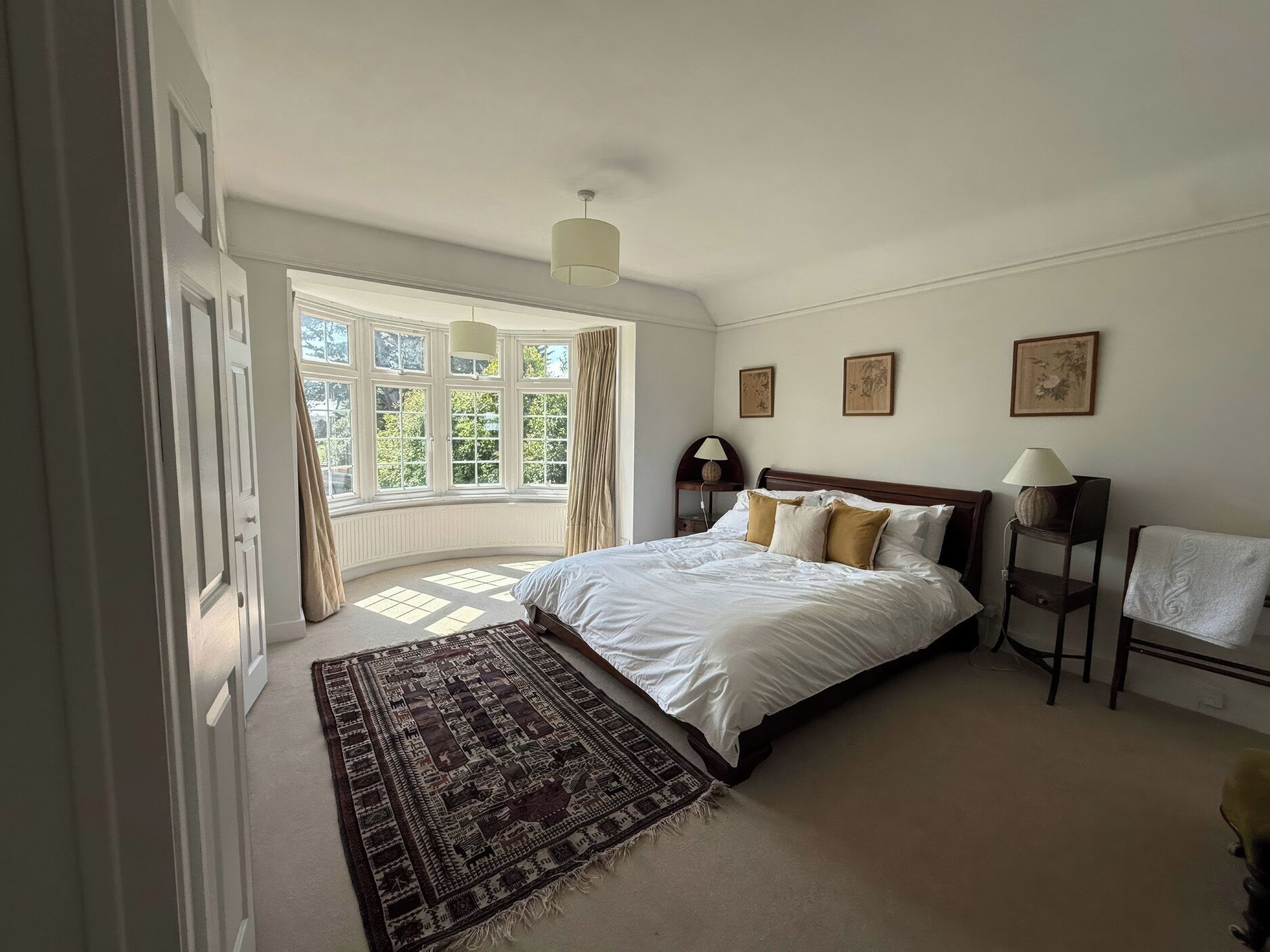 A bedroom with a large bed, a window with curtains, a bedside table with a lamp, and a rug.