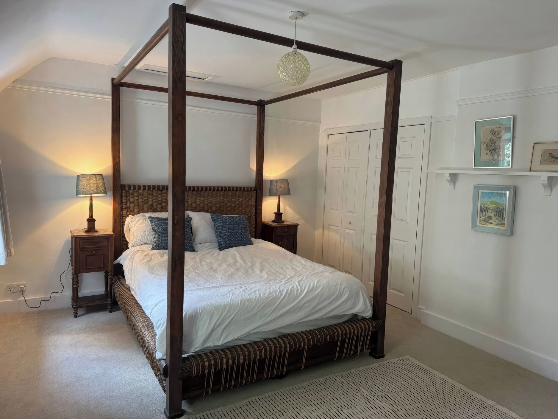 A four-poster bed with a wooden frame, white bedding, and two bedside lamps.