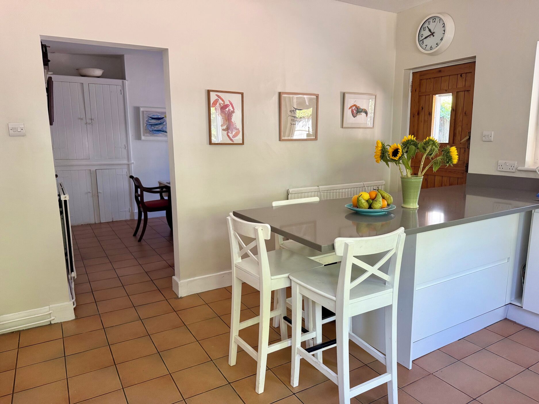 A kitchen with a dining table, chairs, a clock, and framed artwork on the wall.