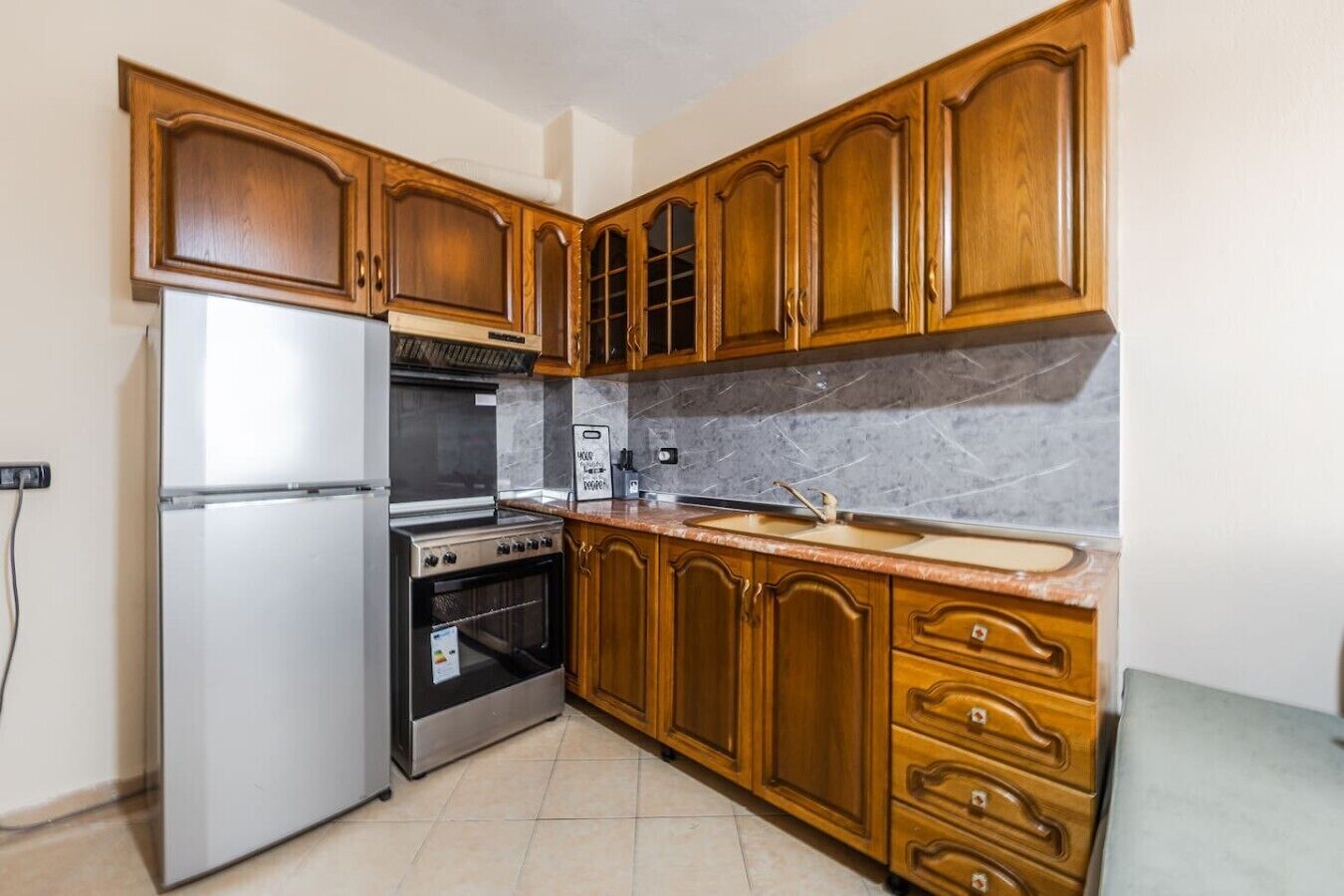 A kitchen with wooden cabinets, a stainless steel refrigerator, a built-in oven, and a marble countertop.
