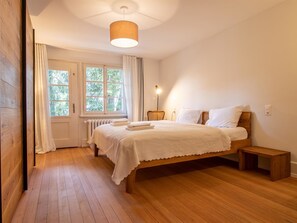 A bedroom with a wooden floor, a bed with white linens, a bedside table, and a window with curtains. - Pradella 1 by Arosa Holiday Appartement/Fewo, Bad, WC Pradella 1 by Interhome (Arosa)