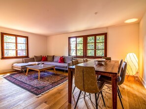 Un salon spacieux avec une table à manger en bois, un canapé et une grande fenêtre donnant sur les arbres.
