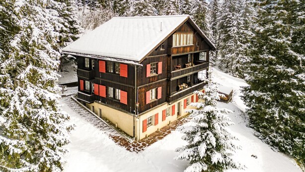 Eine mehrstöckige Holzhütte mit Balkonen, umgeben von schneebedeckten Bäumen.