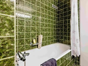 Ein Badezimmer mit grünen Marmorfliesen, einer weißen Badewanne, einer Duschbrause und einem Handtuchhalter.