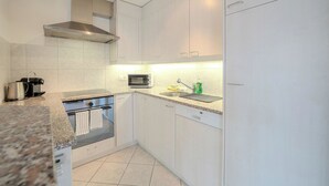 Una cocina moderna con armarios blancos, una campana extractora de acero inoxidable, un microondas y un lavavajillas.