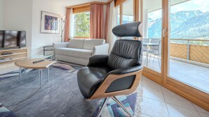 Una sala de estar moderna con un sillón de cuero, un sofá, un televisor y un balcón con vistas a la montaña.