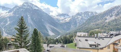 A mountain landscape with a valley, buildings, and a wooden balcony.