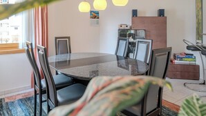 Un comedor moderno con una mesa redonda, sillas, lámparas colgantes y vistas al exterior.
