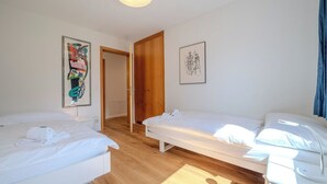 Habitación de hotel con dos camas individuales, suelo de madera, una puerta y dos cuadros enmarcados en las paredes.