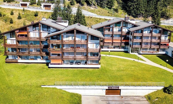 A modern multi-story hotel with balconies, a flat roof, and a grassy lawn. - I dr Rehwiesa B24 by Arosa Holiday Appartement/Fewo,  , 3-Bettwohnung by Interhome (Arosa)