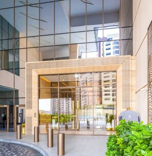 A modern building entrance with glass doors, a metal frame, and a small garden area with plants. - Breathtaking 1BR Palm Tower Nakheel Mall& Sea View (Dubai)