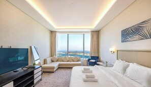 A hotel room with a bed, a sofa, a TV, a desk, and a view of the sea. - Palm Tower Luxury Studio W Stunning Sea View (Dubai)