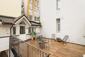 A courtyard with a wooden deck, outdoor seating, and a white building with a tiled roof. - Explore Bergen | 24/7 Self check-in | 500m Torget (Bergen)