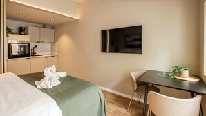 Ein modernes Hotelzimmer mit Bett, Esstisch, Stuhl, Fernseher und einer Küchenzeile.