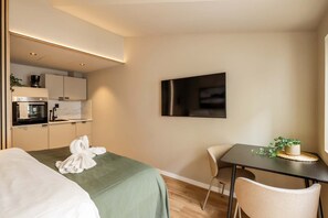 A modern hotel room with a bed, a small dining table, a chair, a TV, and a kitchenette. - Explore Bergen | 24/7 Self check-in | 500m Torget (Bergen)
