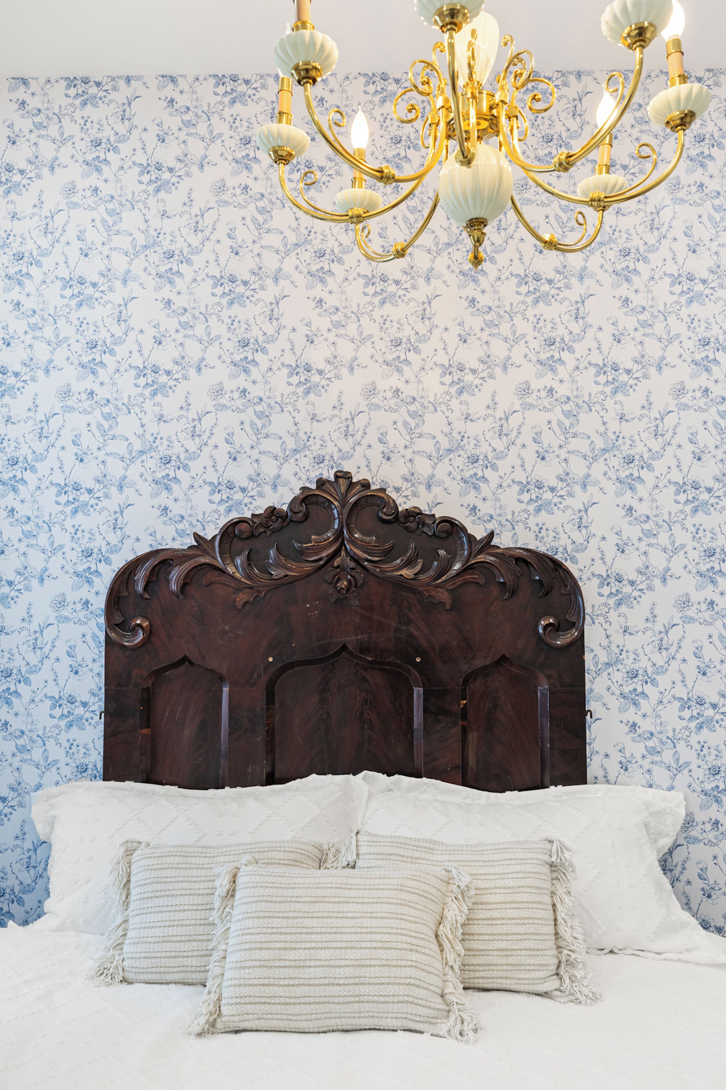 Un dormitorio con cabecera de madera, una araña y papel tapiz floral.