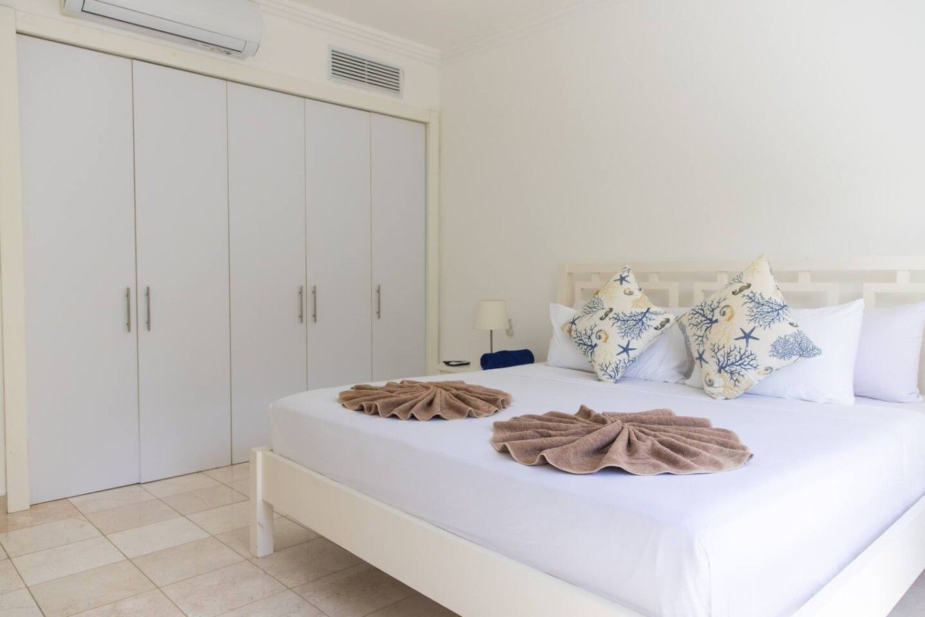 Une chambre d’hôtel avec un lit, des rideaux blancs, une armoire et une table de chevet avec une lampe.