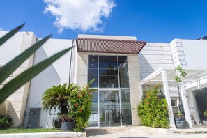A modern building with a large glass entrance, potted plants, and a clear blue sky. - Beach Condo | 2 Pools | Electricity Included (Punta Cana)