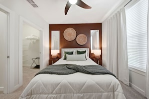 Ein Schlafzimmer mit einem Bett, einem Deckenventilator, zwei Wandleuchten, einem Nachttisch und einem Fenster mit Jalousien.