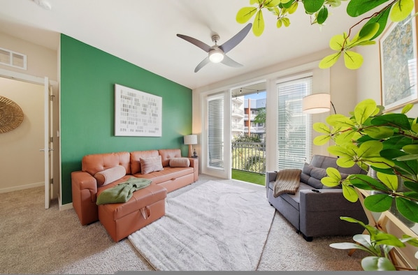 Ein Wohnzimmer mit zwei Sofas, einem Deckenventilator, einer grünen Wand und einem großen Fenster mit Jalousien.