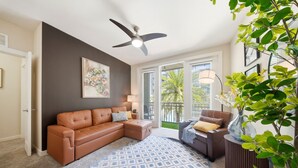 A living room with a brown sectional sofa, a patterned rug, a ceiling fan, and a view through glass doors. - Modern 2BR w/ Pool | Pet-Friendly | Unit #17 (Tampa)