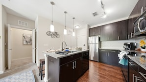 A modern kitchen with dark cabinets, stainless steel appliances, and pendant lighting. - Modern 2BR w/ Pool | Pet-Friendly | Unit #17 (Tampa)