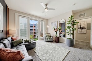 Ein Wohnzimmer mit Sofa, Sessel, Topfpflanze, Deckenventilator und einem großen Fenster.