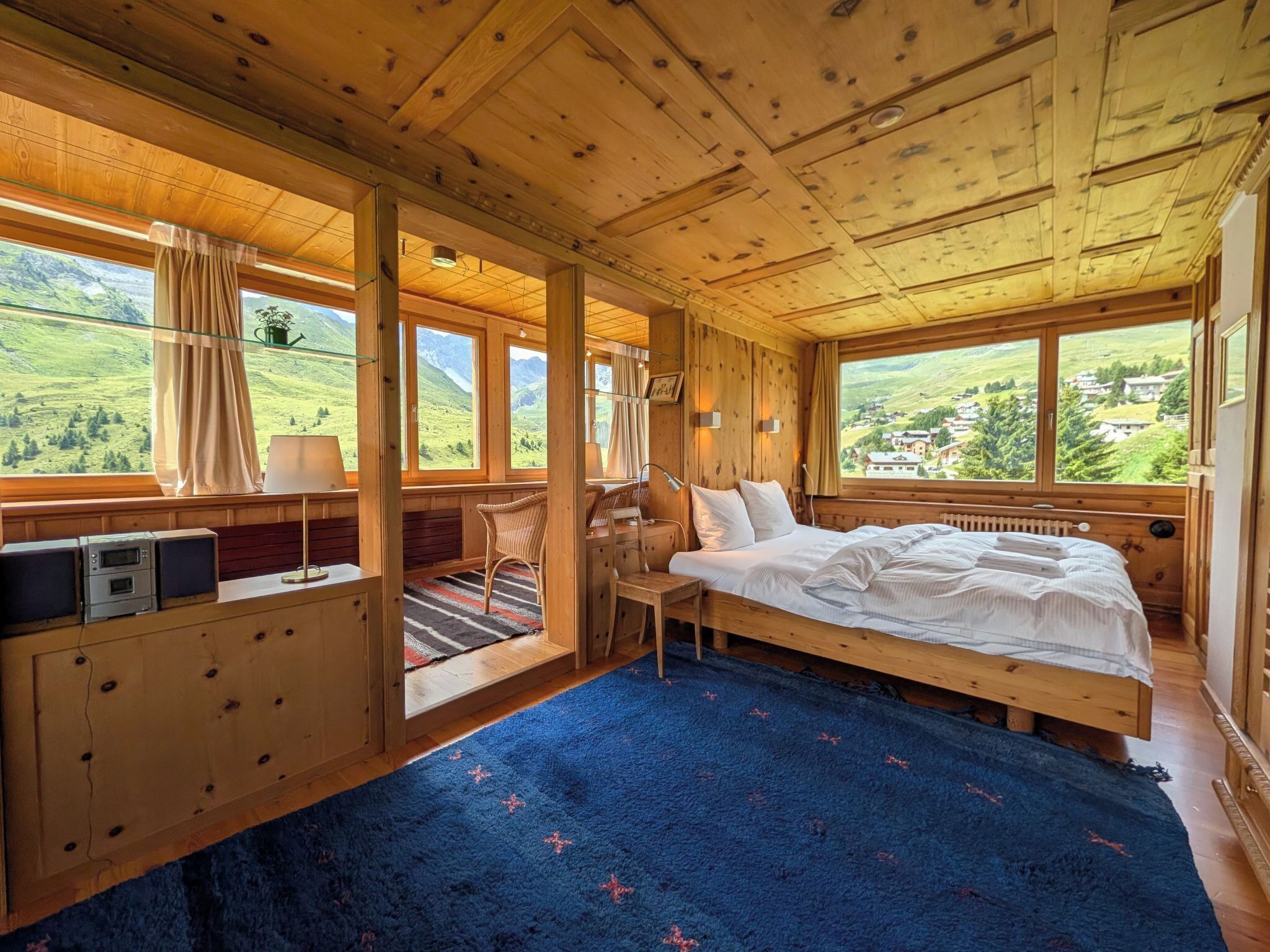 Un dormitorio de cabaña de madera con una cama, un escritorio y vistas a un valle verde.