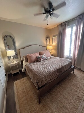 A bedroom with a bed, a nightstand, a mirror, a ceiling fan, and a window with curtains. - Cozy 1-bedroom condo, close to Sabino Canyon and great restaurants (Tucson)