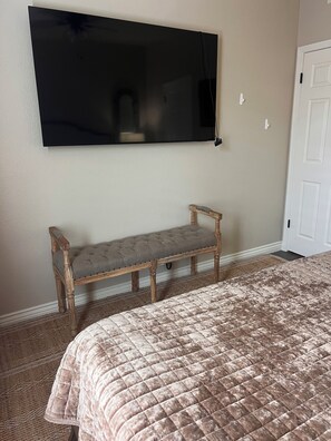 A bedroom with a bed, a bench, a flat-screen TV mounted on the wall, and a door. - Cozy 1-bedroom condo, close to Sabino Canyon and great restaurants (Tucson)